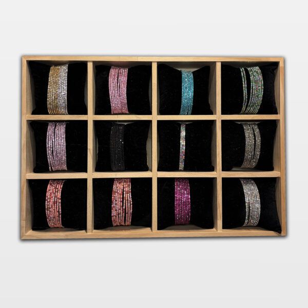 Übersichtsfoto von 12 elastischen Strassarmbändern in verschiedenen Farben – auf schwarzen Kissen in einer Holzbox arrangiert, ideal für Schmuckpräsentation und Farbauswahl.