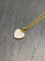 Filigrane goldene Edelstahlkette mit weißem Herzanhänger, Nahaufnahme auf dunklem Schieferhintergrund