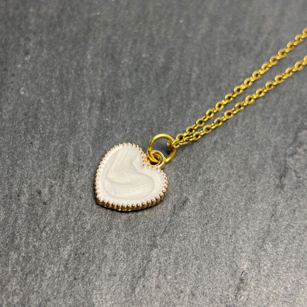 Filigrane goldene Edelstahlkette mit weißem Herzanhänger, Nahaufnahme auf dunklem Schieferhintergrund