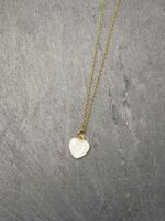 Minimalistische Edelstahlkette in Gold mit weißem Herzanhänger auf dunklem Stein-Hintergrund