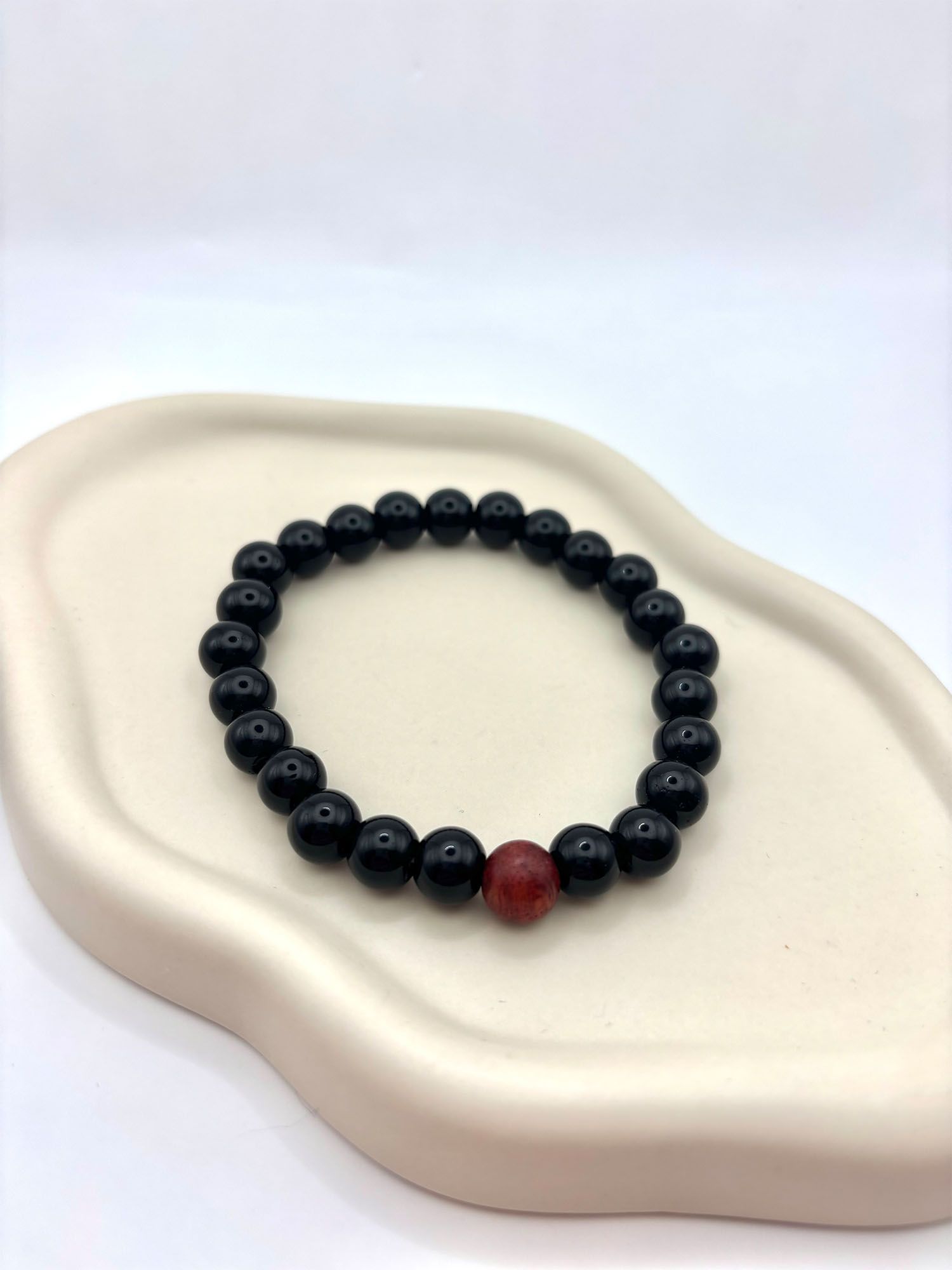 Perlenarmband_Obsidian_mit_Holzperle_liegend_auf_Teller_1 Schwarzes Perlenarmband mit Obsidian und Holzdetail – Bild 1