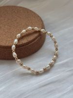 Zartes Armband aus echten Süßwasserperlen und goldfarbenen Hämatitperlen, liegend auf Korkunterlage