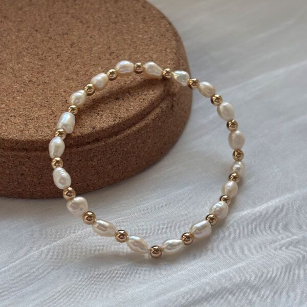 Zartes Armband aus echten Süßwasserperlen und goldfarbenen Hämatitperlen, liegend auf Korkunterlage