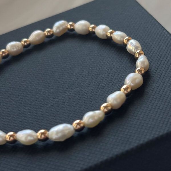 Nahaufnahme von Perlenarmband mit natürlichen Süßwasserperlen und glänzenden Goldperlen