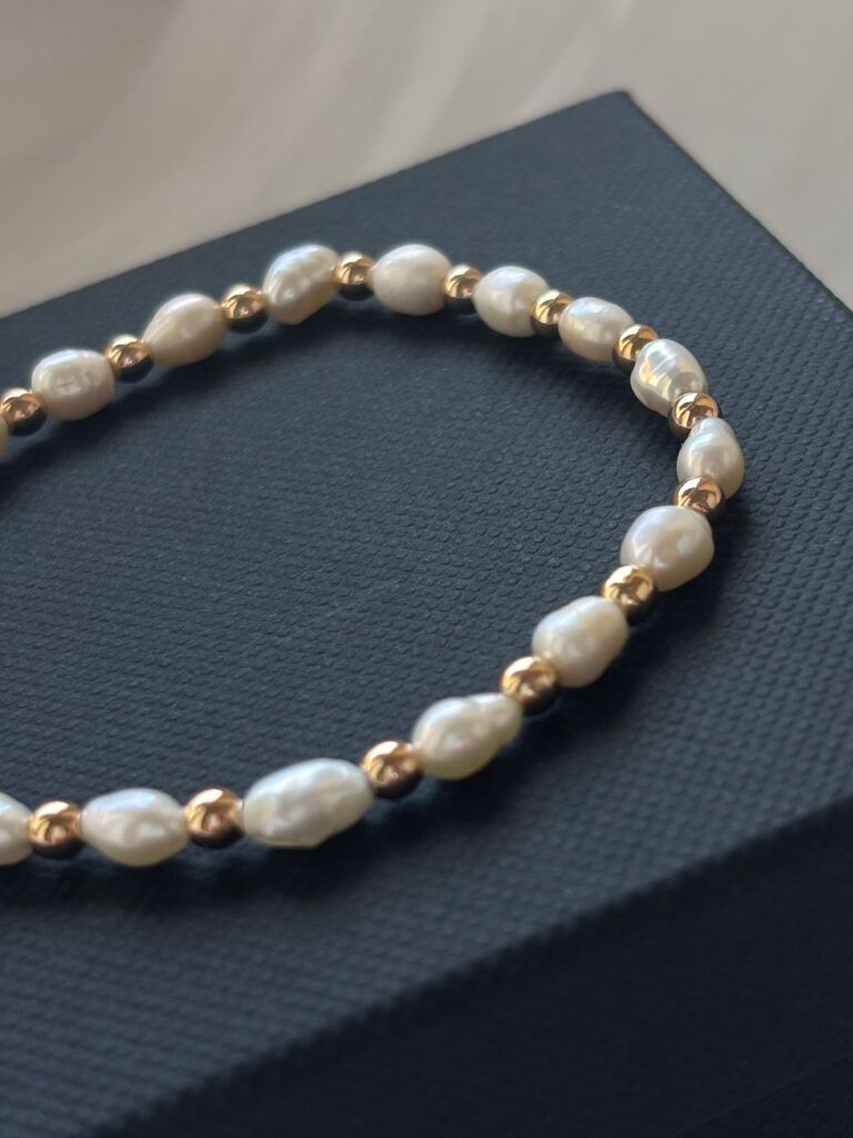 Nahaufnahme von Perlenarmband mit natürlichen Süßwasserperlen und glänzenden Goldperlen