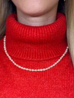 Feine Süßwasser-Perlenkette, getragen am Hals – Detailansicht auf rotem Rollkragen, elegantes Modeaccessoire für Frauen mit klassischem Stil