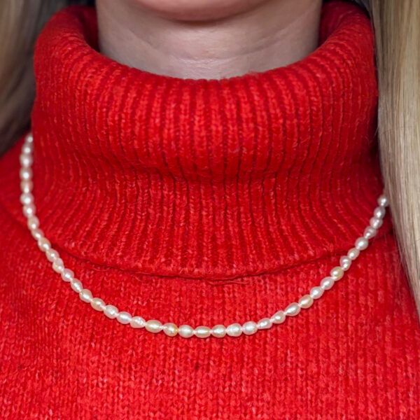 Feine Süßwasser-Perlenkette, getragen am Hals – Detailansicht auf rotem Rollkragen, elegantes Modeaccessoire für Frauen mit klassischem Stil