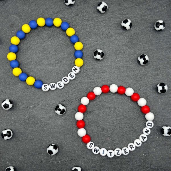 Beaded bracelet spelling SWEDEN in blue and yellow beads, surrounded by small soccer balls on a gray background.
