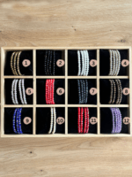 Wooden display tray with twelve compartments holding color-varied beaded bracelets, labeled 1–12 in soft pink circles.