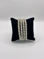 Beaded white faceted bracelet strands draped over a black cushion display stand.