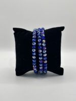 Three strands of faceted blue and purple beaded bracelets resting on a black velvet display pillow.