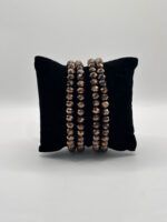 Black velvet cushion with four bronze faceted-bead bracelets draped over the top edge.