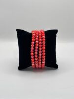 Black velvet pillow with multiple strands of red faceted bead necklaces draped over the top