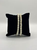 Two strands of faceted white beads draped over a black velvet display pillow
