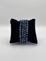Black velvet display pillow wrapped with four strands of faceted blue beads, showcasing jewelry.