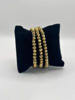 Three gold-toned faceted bead bracelets draped over a black velvet display pillow.