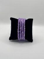 Three strands of faceted purple beads draped over a black velvet pillow.