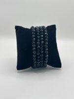 Black multi-strand faceted bead bracelet displayed on a dark velvet pillow jewelry stand