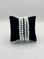 Three strands of pale, faceted white beads draped over a black velvet display pillow.