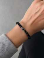 Wrist with a black beaded bracelet and silver spacers resting on a gray sleeve.