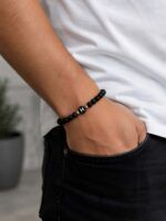 Close-up of a forearm wearing a black beaded bracelet with a single bead bearing the white letter 'H'.?