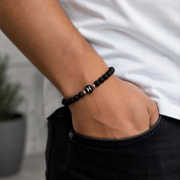 Close-up of a forearm wearing a black beaded bracelet with a single bead bearing the white letter 'H'.?