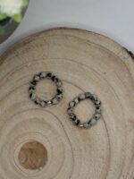 Beaded bracelet with gray speckled beads and a small gold 'LOVE' charm on a circular wood slice surface.