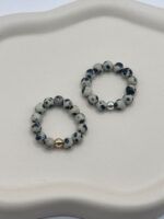Beaded bracelet with speckled gray and black stones and a gold accent bead on a white surface.