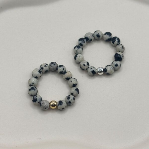 Beaded bracelet with speckled gray and black stones and a gold accent bead on a white surface.