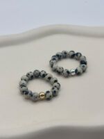 Beaded bracelet with speckled gray and white stones and a single gold bead on a light surface
