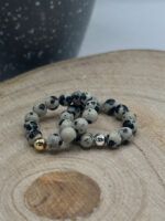 Beaded bracelet made of gray and black speckled stones with gold and silver accent beads on a wooden surface.