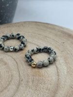 Beaded grey marbled gemstone bracelet with a single gold bead resting on a light wooden surface.