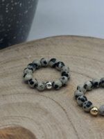 Beaded bracelet with gray marbled stones and a silver clasp resting on a wooden surface.