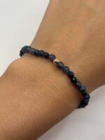 Close-up of a wrist wearing a dark blue faceted beaded bracelet with a small gold bead accent.