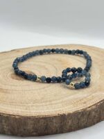 Blue beaded bracelet with gold spacers resting on a wooden tree slice, close-up product shot