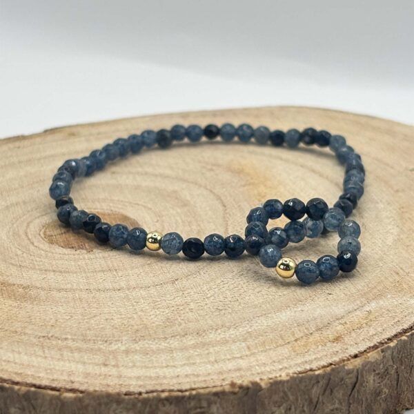 Blue beaded bracelet with gold spacers resting on a wooden tree slice, close-up product shot