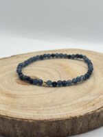Dark blue beaded bracelet with two small gold accent beads resting on a wooden log slice surface.