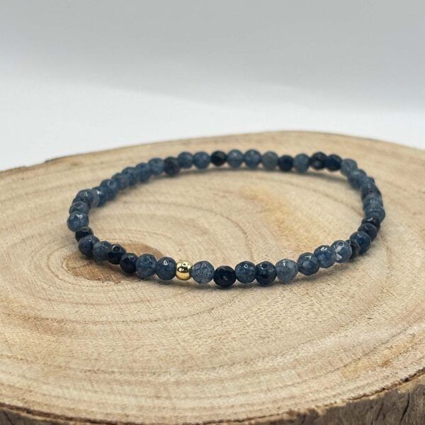 Dark blue beaded bracelet with two small gold accent beads resting on a wooden log slice surface.