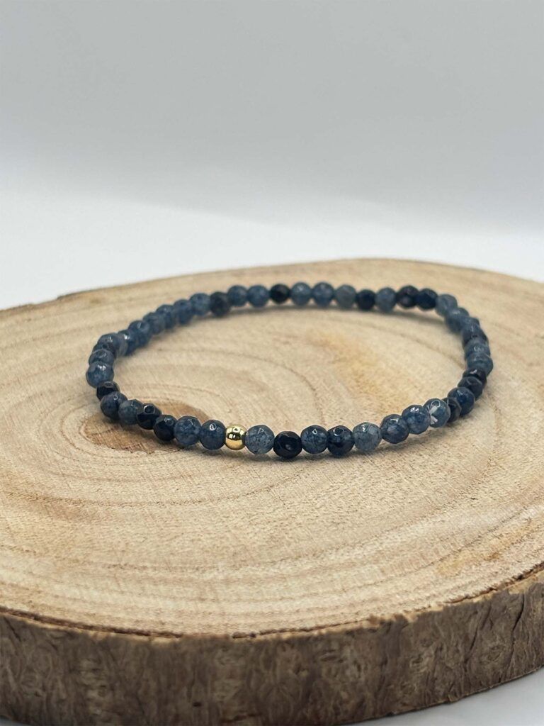 Dark blue beaded bracelet with two small gold accent beads resting on a wooden log slice surface.