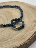 Beaded navy bracelet with a single gold spacer bead resting on a round wooden surface.